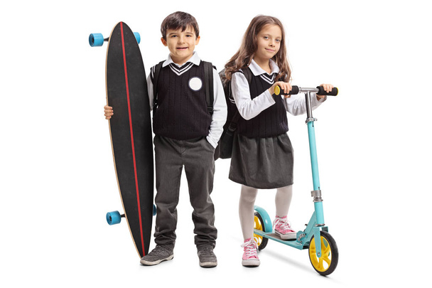 Full length portrait of a schoolboy with a longboard and a schoolgirl with a scooter isolated on white background - Foto, Imagem