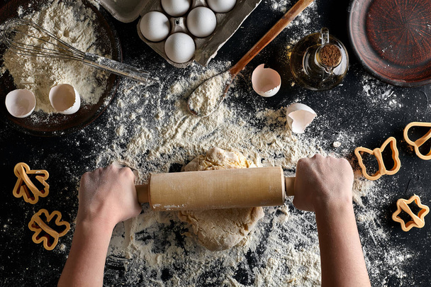 Female hands rolling dough with a rolling pin on a black table. Top view - 写真・画像