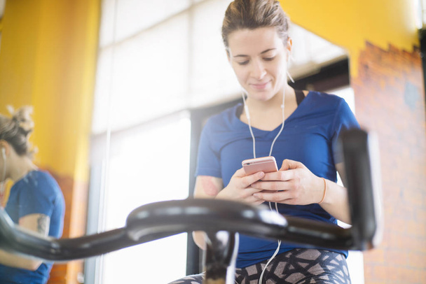 Woman practicing spinning at the gym  with smartphone - Foto, afbeelding