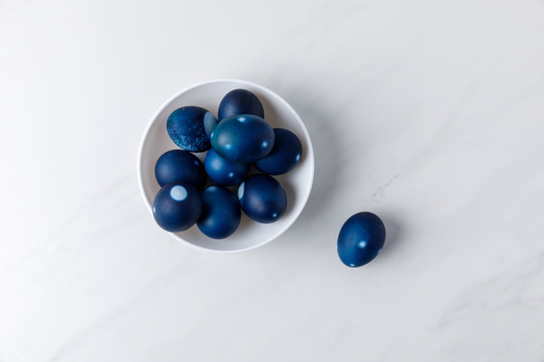 top view of blue painted easter eggs in bowl on white surface - Foto, Imagem
