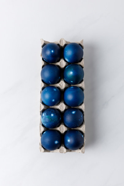 vista superior de ovos de páscoa pintados de azul na bandeja de ovos na mesa branca
 - Foto, Imagem