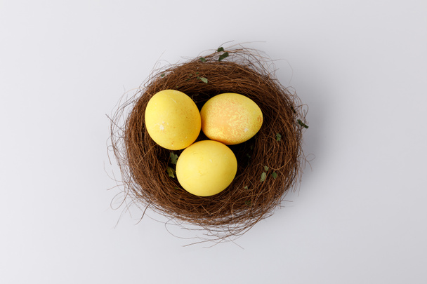 top view of yellow painted easter eggs in decorative nest on white - Photo, image