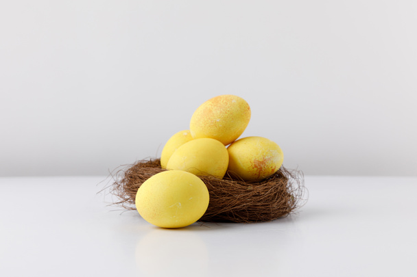 oeufs de Pâques peints en jaune dans un nid décoratif sur une table blanche
 - Photo, image