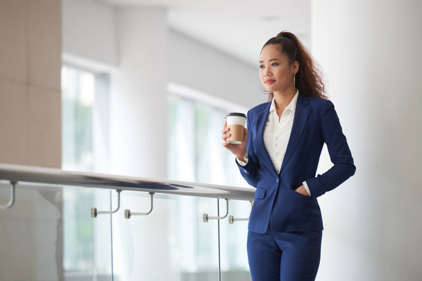 Pensive young Asian business lady drinking coffee - 写真・画像