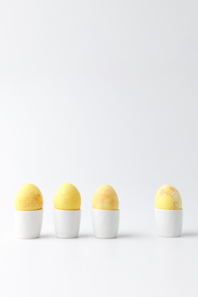 four yellow painted easter eggs in egg stands on white - Foto, Bild