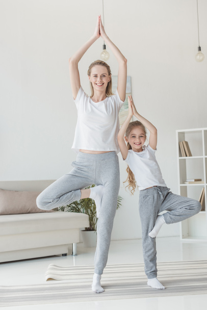 happy mother and daughter balancing in tree pose together - Valokuva, kuva