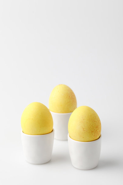 tres huevos de Pascua pintados de amarillo en soportes de huevo sobre blanco
 - Foto, imagen