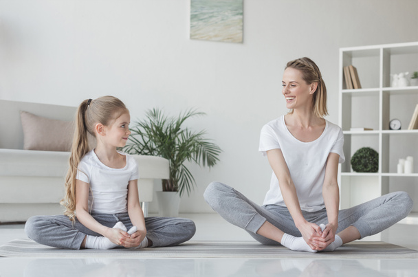 madre e hija practicando yoga en pose de mariposa en casa
 - Foto, Imagen