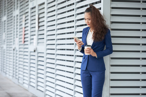 Business lady drinking coffee and checking messages in her smartphone - Фото, зображення