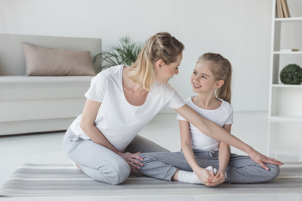 mother teaching daughter how to sit in yoga butterfly pose - Fotoğraf, Görsel