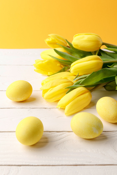 ovos de páscoa pintados de amarelo com buquê de tulipas em mesa de madeira
 - Foto, Imagem