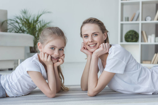 happy mother and daughter lying on floor together and looking at camera - Foto, Bild
