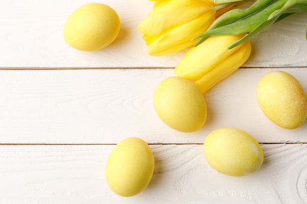 top view of yellow painted easter eggs with tulips on wooden table - Photo, Image
