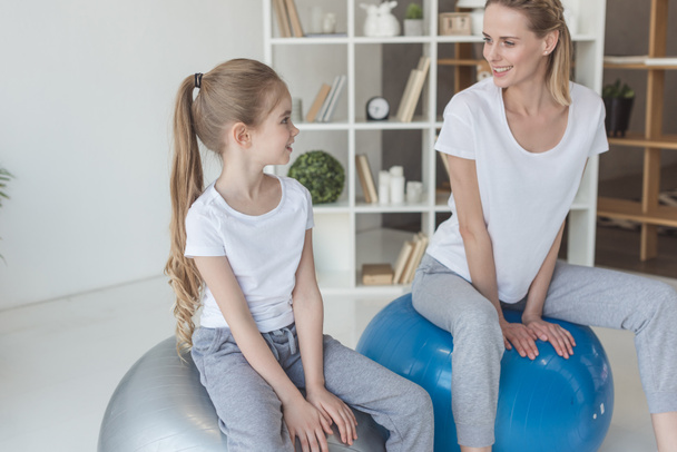 happy mother and daughter sitting on fit balls at home and looking at each other - Фото, изображение