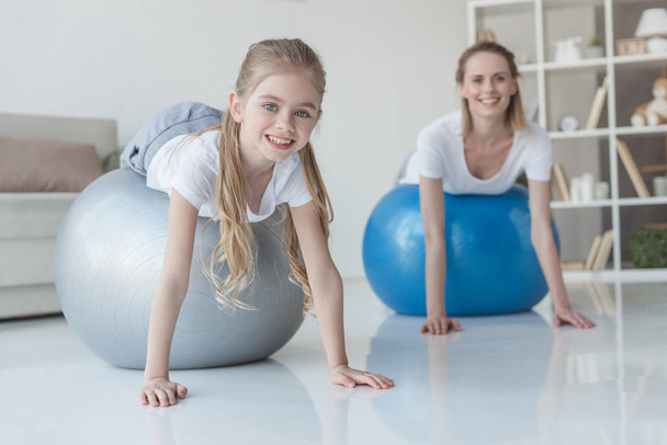 smiling mother and daughter lying on fit balls at home - Foto, imagen