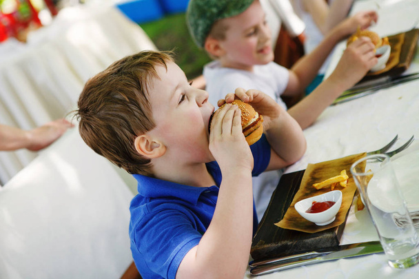 kleine jongen eten van een hamburger in een cafe, voedsel concept - Foto, afbeelding