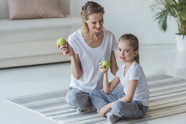 feliz madre e hija comiendo manzanas en el suelo
 - Foto, Imagen