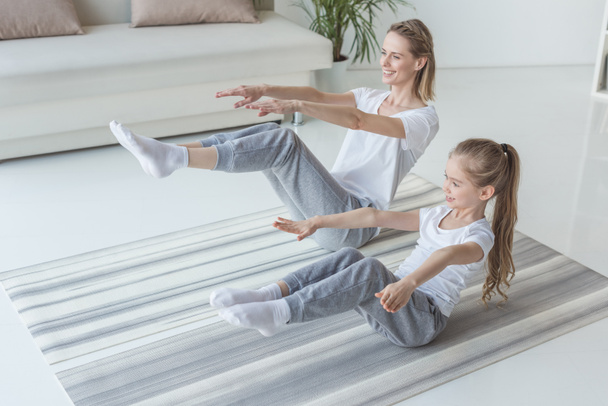 mother and daughter doing v-sit crunches on yoga mat - Foto, Bild