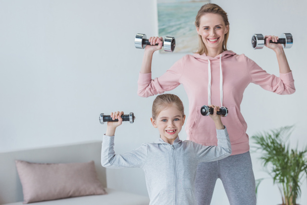 fit mother and daughter working out with dumbbells at home - Photo, Image