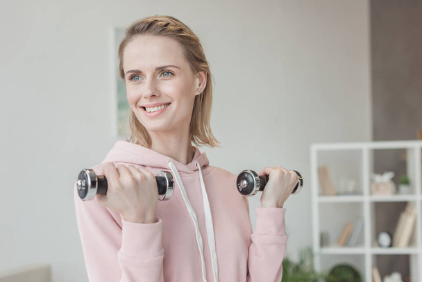 attractive smiling woman working out with dumbbells at home - Foto, Imagem