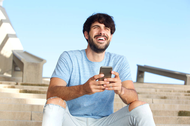 Portret als gelukkig man zitten buiten met mobiele telefoon - Foto, afbeelding