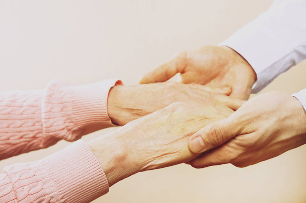 Mature female in elderly care facility gets help from hospital personnel nurse. Close up of aged wrinkled hands of senior woman. Grand mother everyday life. - Foto, Bild
