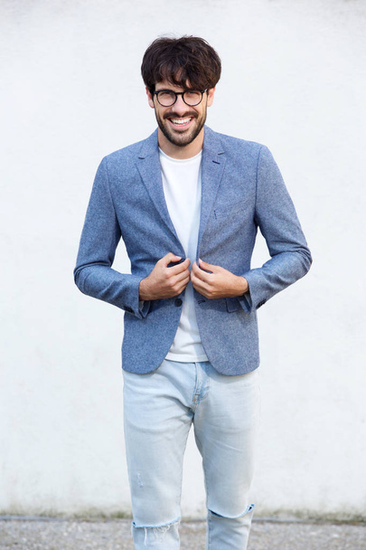 Portrait of happy young man with glasses standing abasing white wall - Fotó, kép