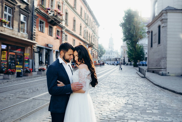 Sensual outdoor portrait. Pretty young couple of newlyweds is gently hugging in the sunny town street. - Fotografie, Obrázek