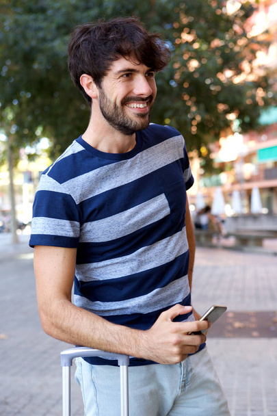 Porträt eines glücklichen männlichen Reisenden, der mit Handy draußen steht - Foto, Bild