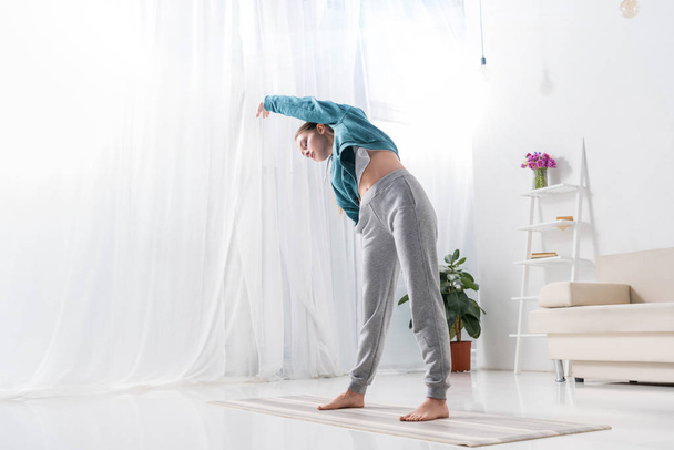 hermosa chica estiramiento en yoga mat en casa
 - Foto, imagen
