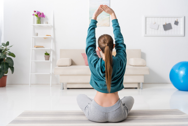 Rückansicht eines Mädchens, das in Lotusposition sitzt und zu Hause Yoga macht - Foto, Bild