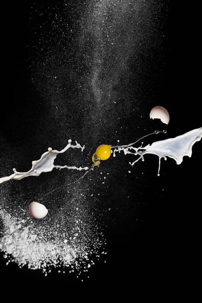 Egg in flight, milk and flour on black background. Scattering egg shells - Фото, изображение
