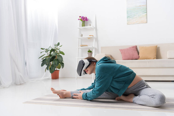chica atlética estiramiento con auriculares de realidad virtual en estera de yoga en casa
 - Foto, imagen