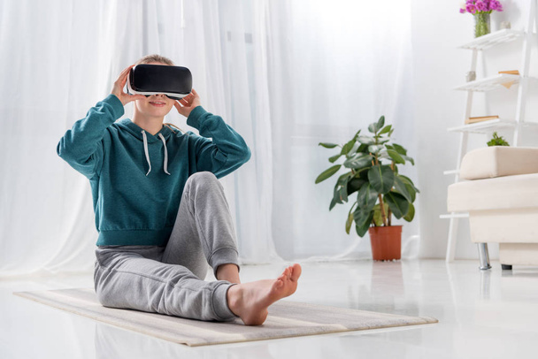 menina sentada no tapete de ioga com fone de ouvido realidade virtual em casa
 - Foto, Imagem
