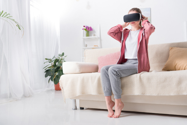 evde kanepenin üzerinde sanal gerçeklik kulaklık giyen kız - Fotoğraf, Görsel