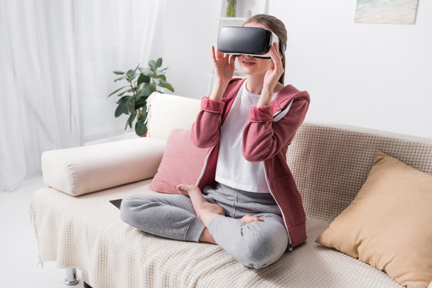 meisje zit in de lotuspositie met virtual reality headset thuis - Foto, afbeelding