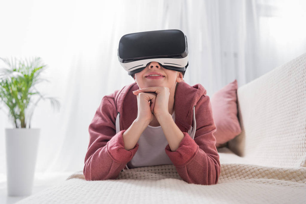 girl lying on sofa and watching something with virtual reality headset at home - Photo, Image