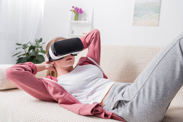 Tyttö tekee istuu kanssa virtuaalitodellisuus kuulokkeet sohvalla kotona
 - Valokuva, kuva