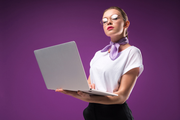 girl holding laptop and looking at camera isolated on purple - Photo, Image