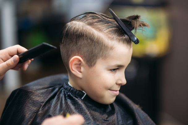 Menino em um corte de cabelo no barbeiro senta-se em uma cadeira
 - Foto, Imagem