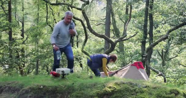 Senior couple have returned back to their tent after a hike. The woman goes in to the tent and the man starts getting the gas stove ready for tea.  - Video