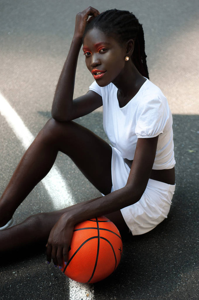 Beautiful ethnic afro-american girl in white with orange basketball - 写真・画像