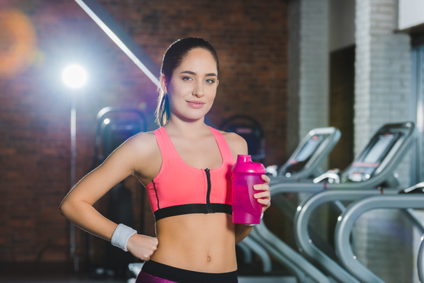 sporty woman standing with shaker in hand against treadmills  - Photo, Image