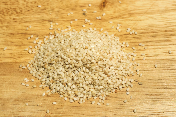Uma pilha de sementes de gergelim natural orgânico seco fecha-se no fundo da placa de madeira
 - Foto, Imagem