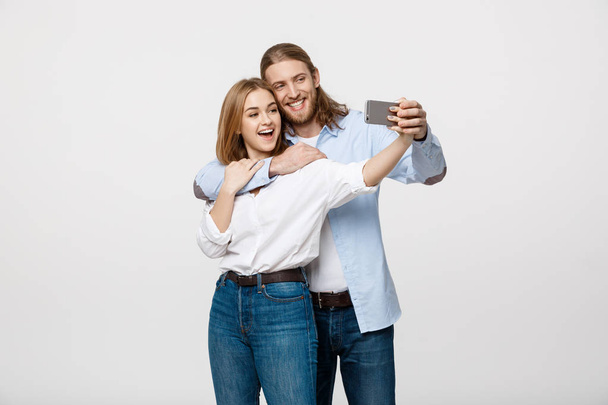 Portrait of a happy couple making selfie photo with smartphone over isolated white studio background. - Photo, Image