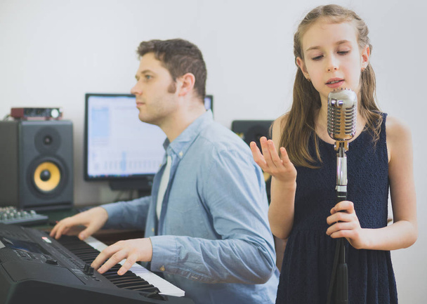 Чоловік з маленькою дівчинкою репетирує пісню в музичній студії. Орієнтована на дівчину
. - Фото, зображення