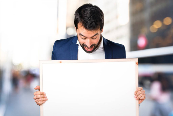 Handsome man holding an empty placard on unfocused background - Photo, Image