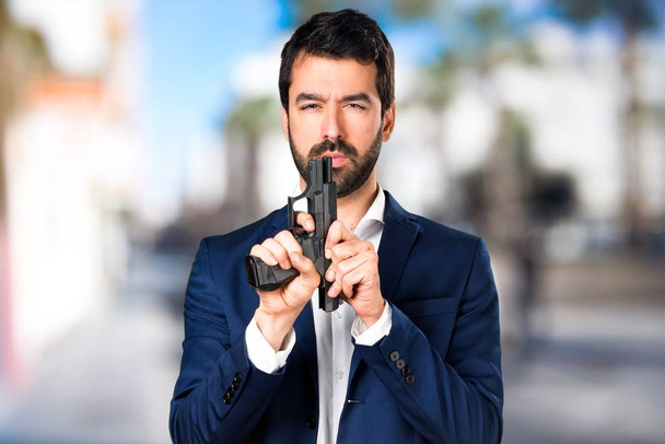 Hombre guapo sosteniendo una pistola sobre un fondo desenfocado
 - Foto, imagen