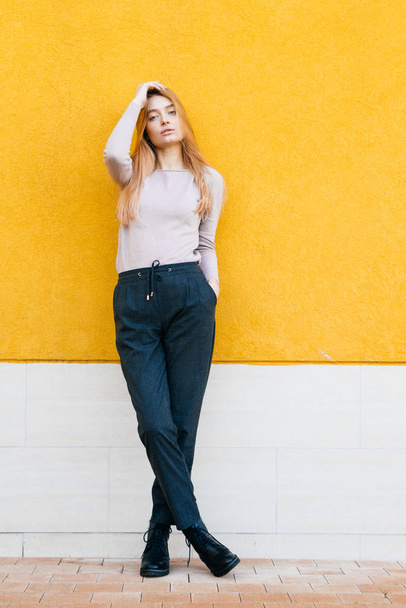 stylish young blond model girl in trendy clothes posing against a yellow wall - Photo, Image