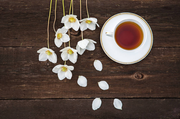 A cup with tea, white flowers of anemones on a wooden background - Foto, Bild